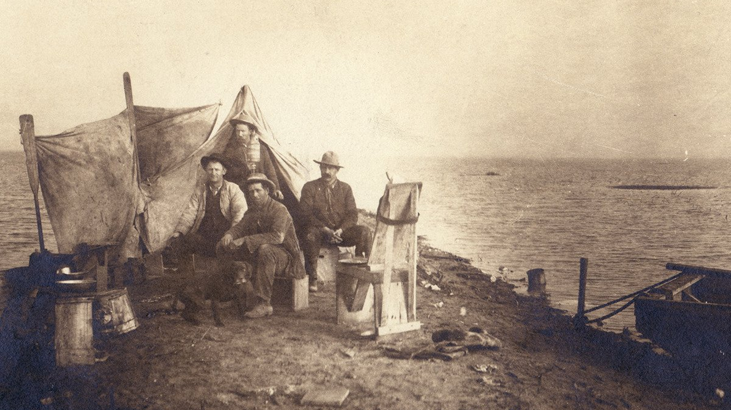 A group of unidentified men and a dog camping at the shores of Tulare Lake circa 1880. It is one of two photographs which survive of the historic lake.