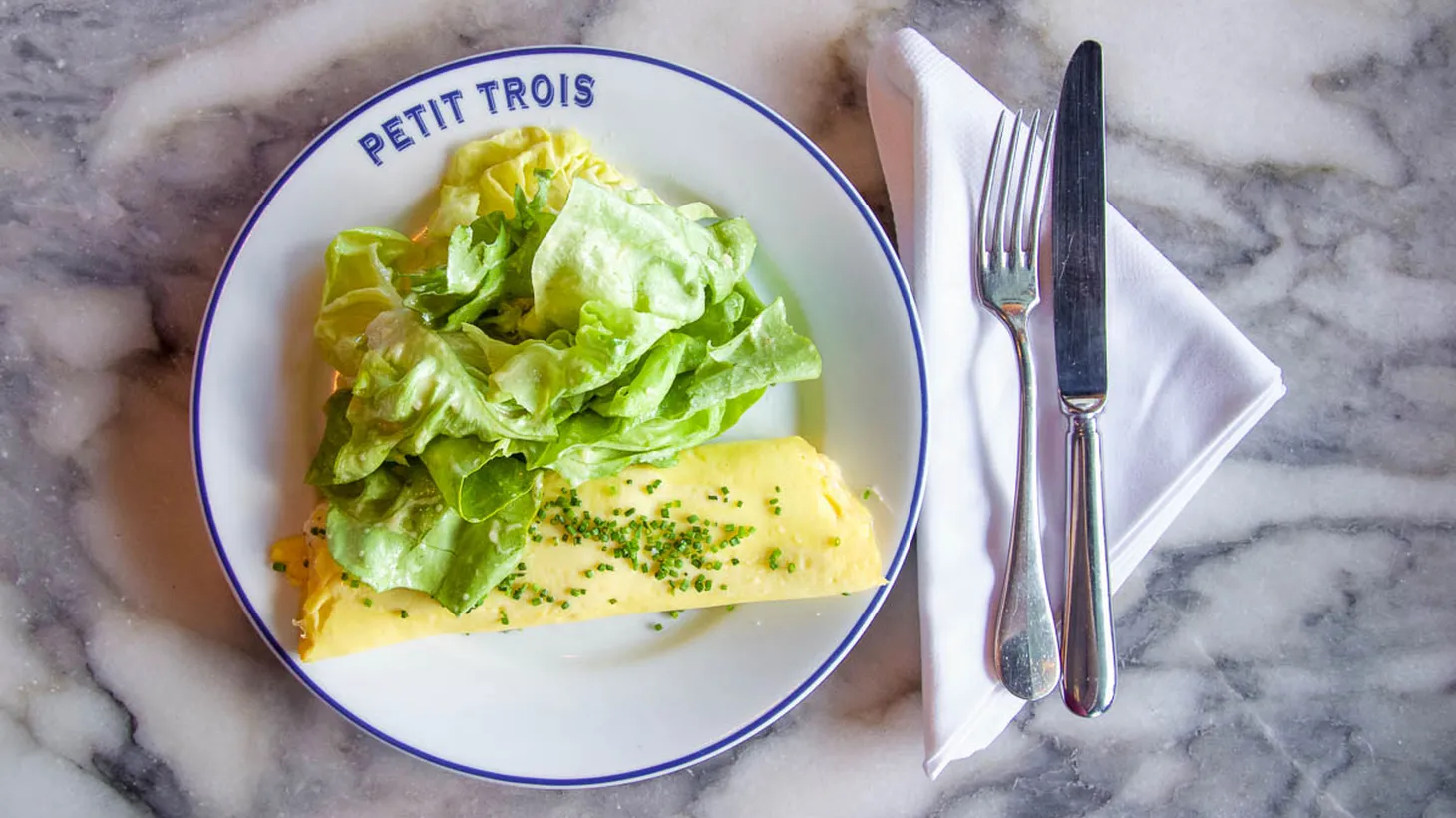 The omelet at Petit Trois, made with three eggs, butter, salt, white pepper, Boursin, and chives, is served with a simple side salad.