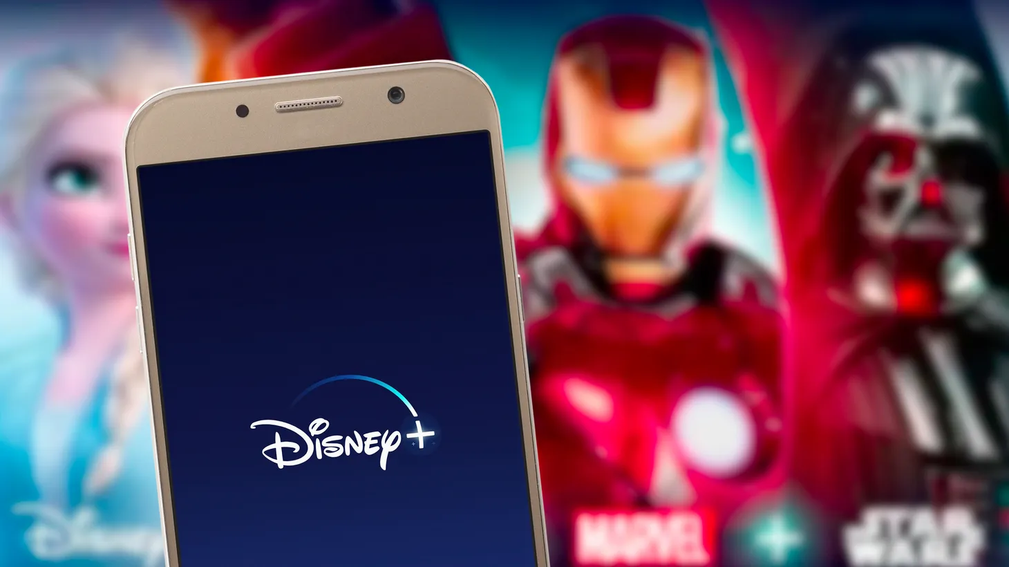 A Marvel poster appears behind a Disney+ app logo on a smartphone screen. Photo by Miguel Lagoa/Shutterstock.