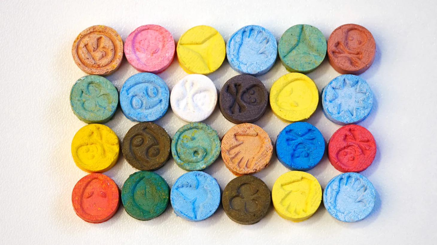 Several pills of MDMA sit on a white table. MDMA releases serotonin rather than mimicking the effects of serotonin, explains psychiatry professor Matthew Johnson.