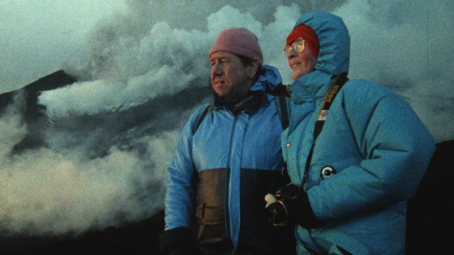 “I firmly believe that [the Kraffts knew] that at any moment could be their last, and that propelled them towards this beautiful, deeply meaningful life where they boldly pursued what they loved most in the world, which were volcanoes,” says filmmaker Sara Dosa. Maurice and Katia Krafft gaze upon a volcano in the distance as smoke and ash swirl behind them.