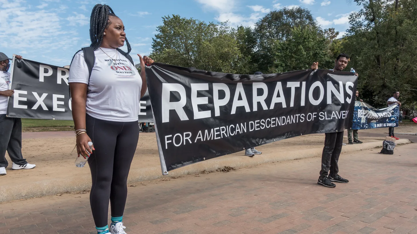 Activists hold a sign demanding reparations.