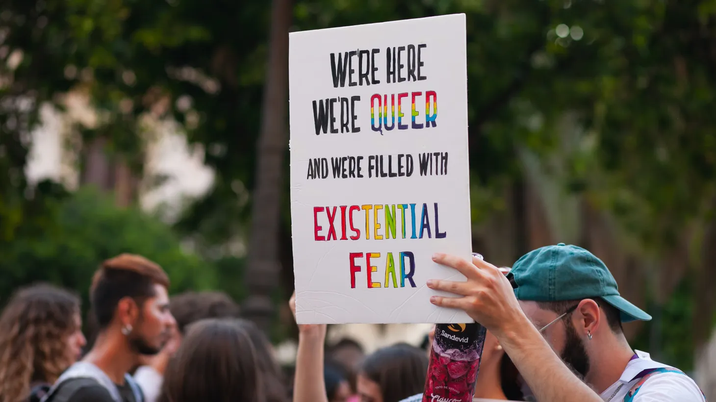 An activist holds a sign that says, “We’re here, we’re queer, and we’re filled with existential fear.”