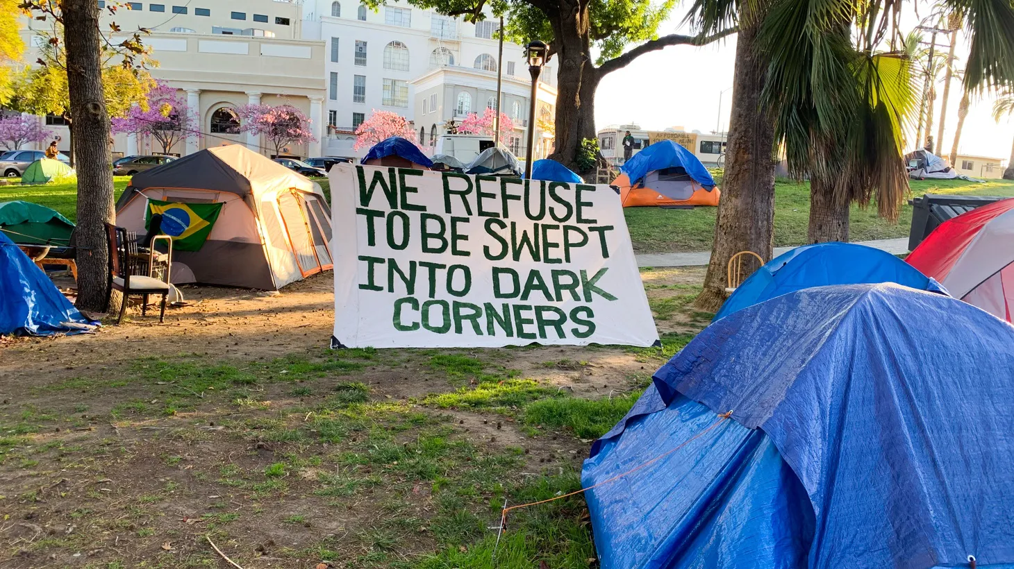 A sign by homeless camps at Echo Park Lake says, “We refuse to be swept into dark corners.” March 24, 2021.