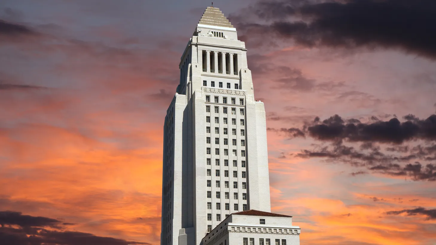 LA City Hall is seen against a sunrise sky.