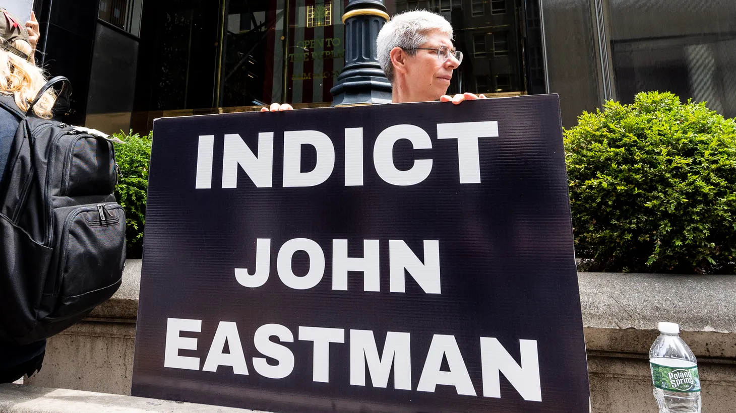 A person holds a sign saying "indict John Eastman" in front of Trump Tower in New York City at a rally, July 6, 2022.