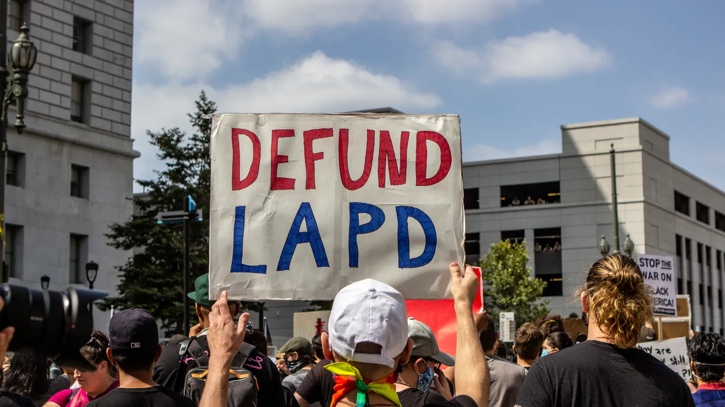 An activist holds a sign saying “defund LAPD.”
