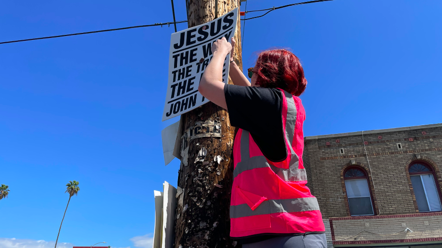 Anya Overmann, who volunteers as an “atheist street pirate,” removes a religious sign on a public telephone pole on Pico Blvd.
