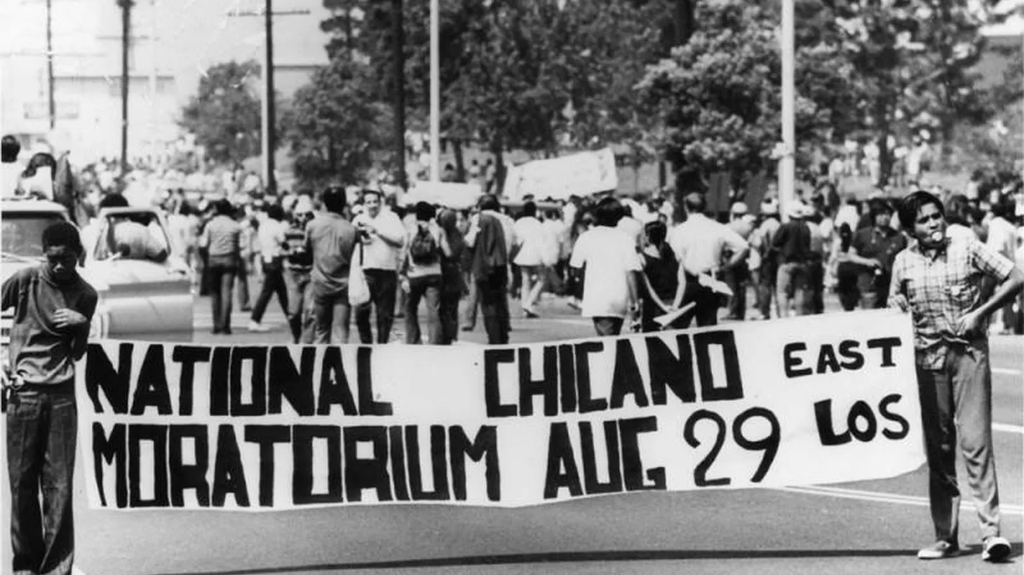 Two young men hold a banner that says "National Chicano Moratorium, East Los Angeles, August 29."