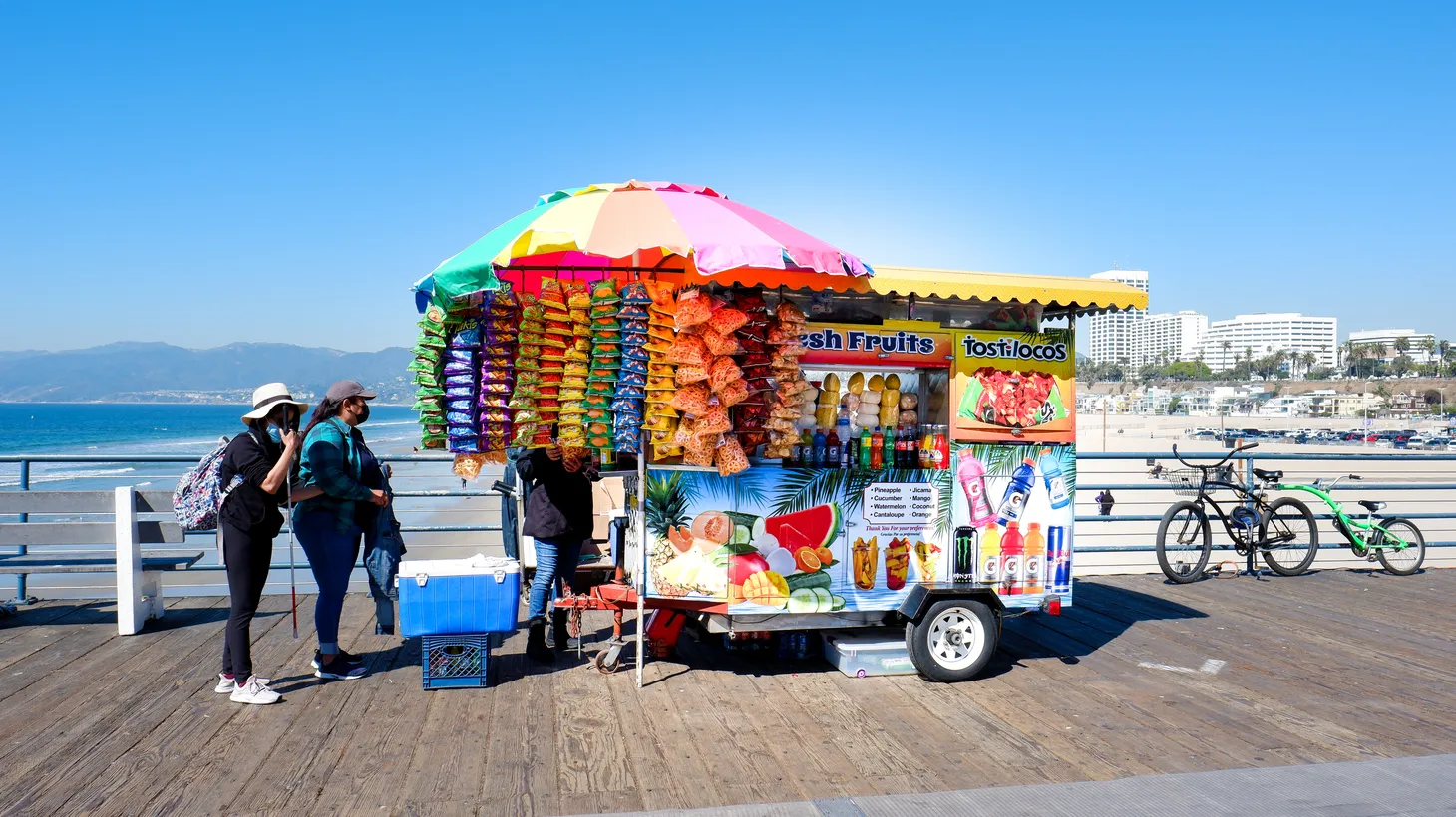 Two customers check out goods from a food cart selling fruit, chips, and cold drinks on the Santa Monica pier. Gov. Gavin Newsom recently signed a law that gives vendors a clearer path to operating legally.