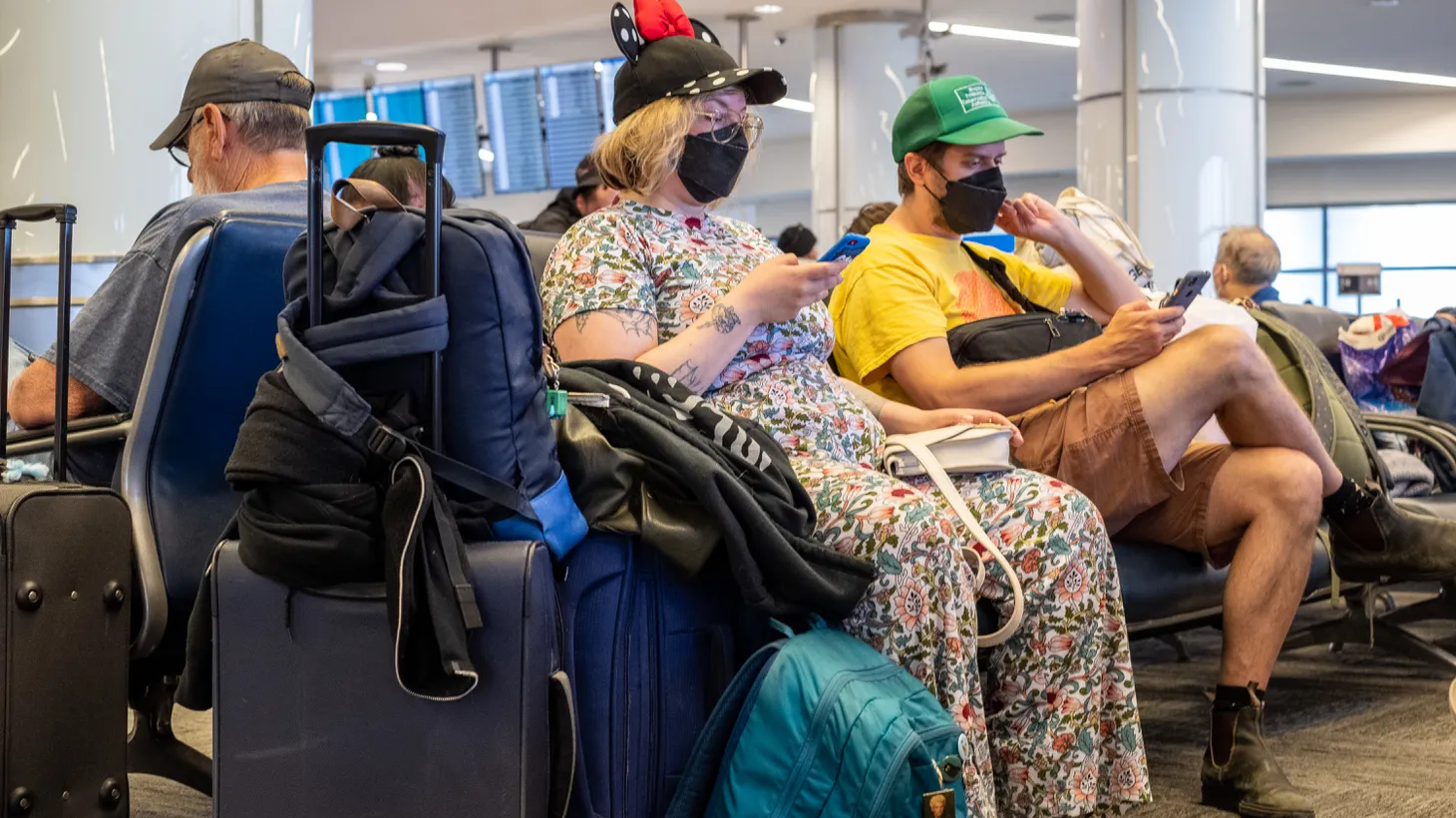 A woman wears a face mask and Minnie House hat while waiting to board a flight at LAX airport, May 22, 2022. Summer is usually travel season, but the COVID forecast doesn’t look promising since cases are up in the state.
