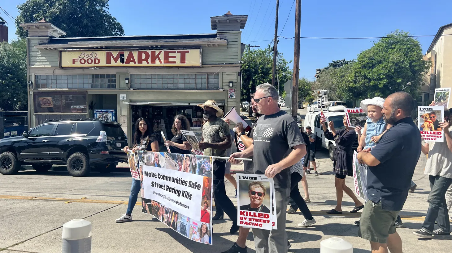 Angelino Heights residents carry signs saying “I was killed by street racing” and “make communities safe, street racing kills,” as they march in front of Bob’s Food Market, aka Toretto's Market & Deli from “The Fast and the Furious.”