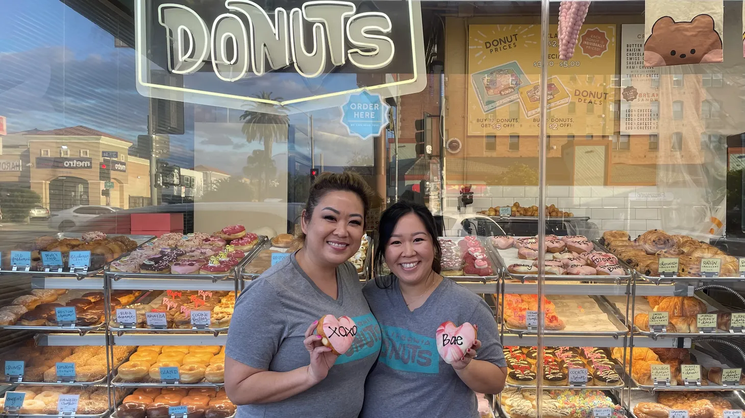 Sisters Danette Kuoch (left) and Steppie Kudo hold heart-shaped donuts in front of their shop, California Donuts #21 in Koreatown.