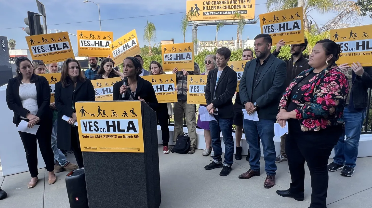 Supporters of the traffic safety ballot measure HLA, including members of the Los Angeles City Council, hold a press conference along Vermont Avenue, where many pedestrian deaths have occurred. Behind the speakers is a billboard sponsored by the Yes on HLA campaign.