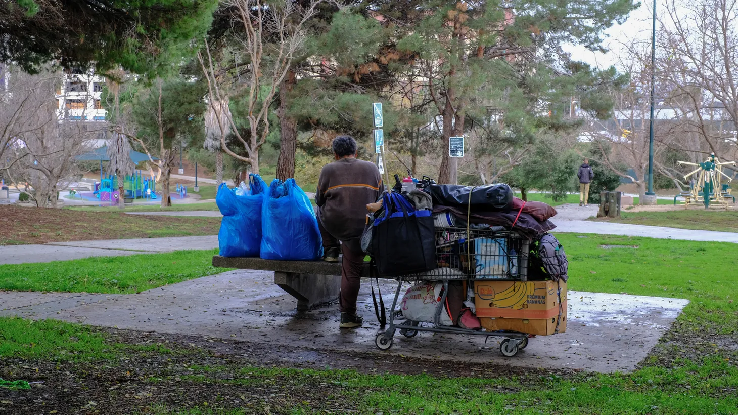 An unhoused person stands with their belongings at a table in Pan Pacific Park in the Fairfax neighborhood of Los Angeles, CA.