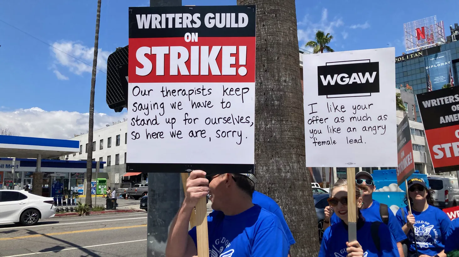 Hollywood writers on strike carry signs that say, “Our therapists keep saying we have to stand up for ourselves, so here we are, sorry,” and “I like your offer as much as I like an angry female lead,” May 2, 2023 in Los Angeles.