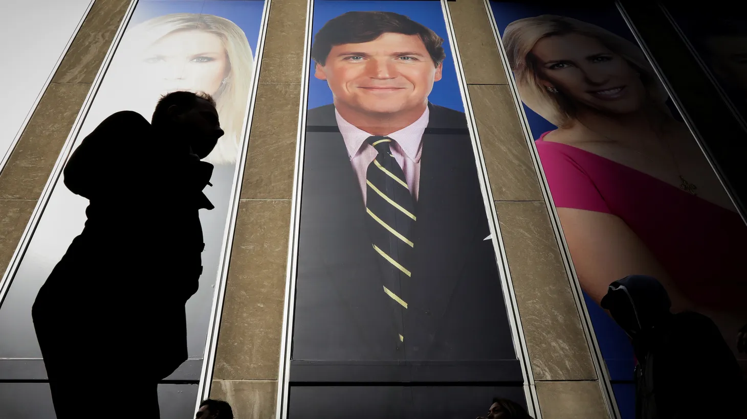 People pass by a promo of Fox News host Tucker Carlson on the News Corporation building in New York, U.S., March 13, 2019.