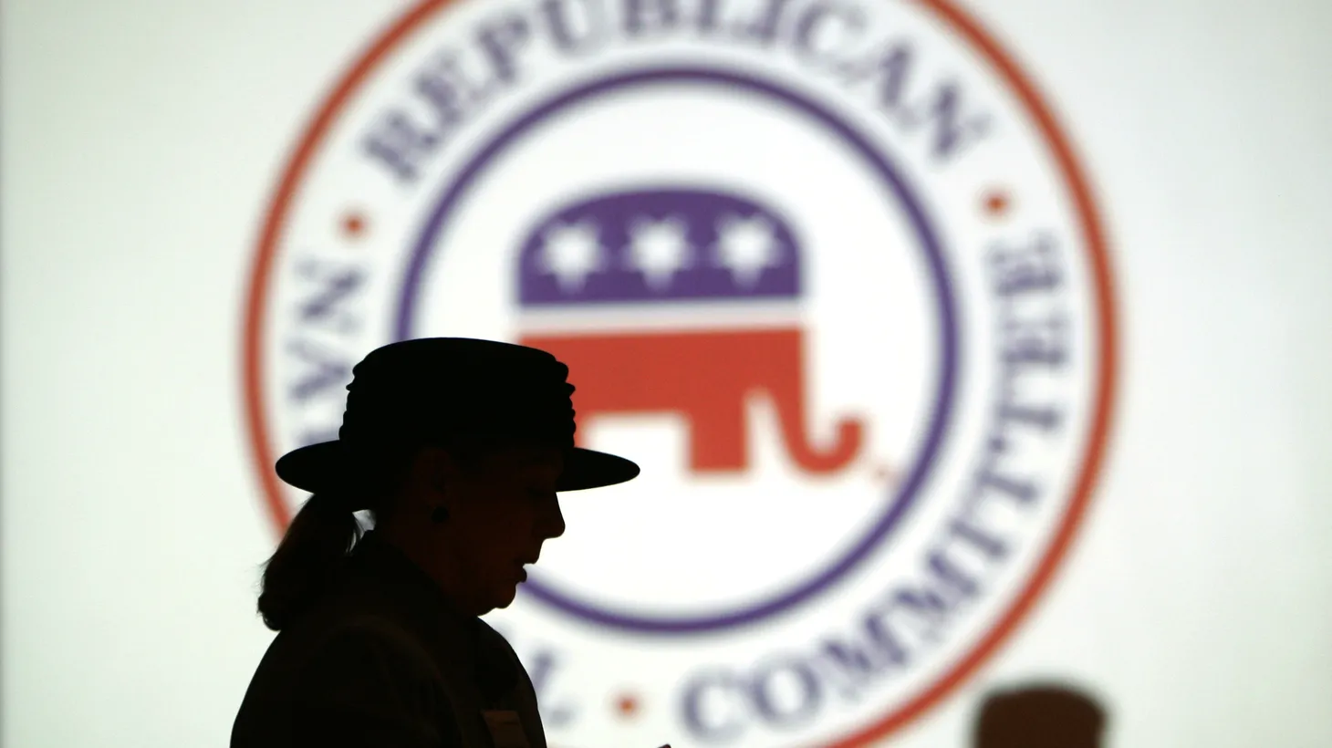 Republican Party members are silhouetted against the Republican National Committee (RNC) logo.