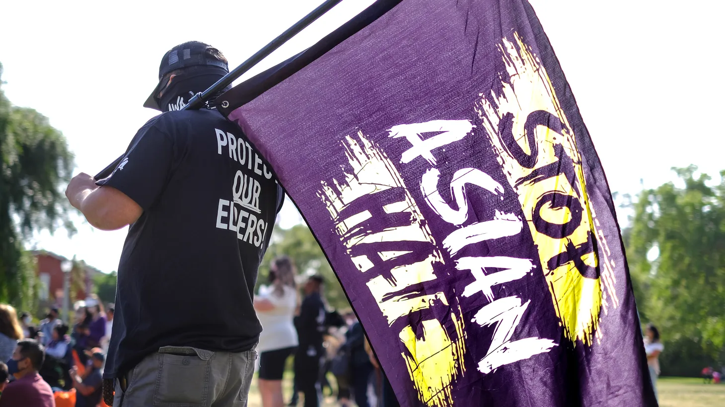A man holds a flag that says, “STOP ASIAN HATE,” while wearing a t-shirt that says, “Protect your elders,” at a rally in the San Gabriel Valley, California, May 22, 2021.