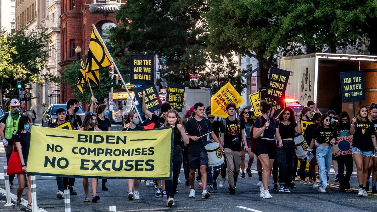 Climate activists march in Washington D.C., carrying signs that say, “Biden: No compromises, no excuses,” “For the air we breathe,” “For the water we drink.”