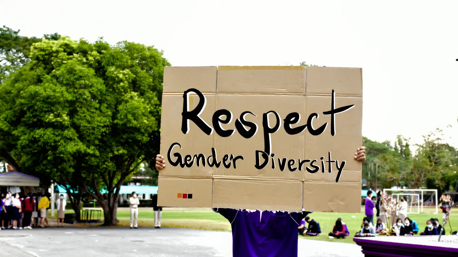 A person on a green courtyard holds a sign saying “respect gender diversity.”