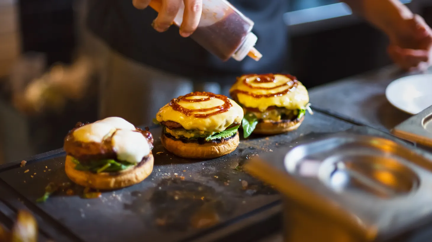 A cook adds sauce to burgers. Fast food workers could see wages rise to as much as $22 per hour by next year, thanks to the FAST Recovery Act. The law applies to fast food chains that have at least 100 locations nationwide.