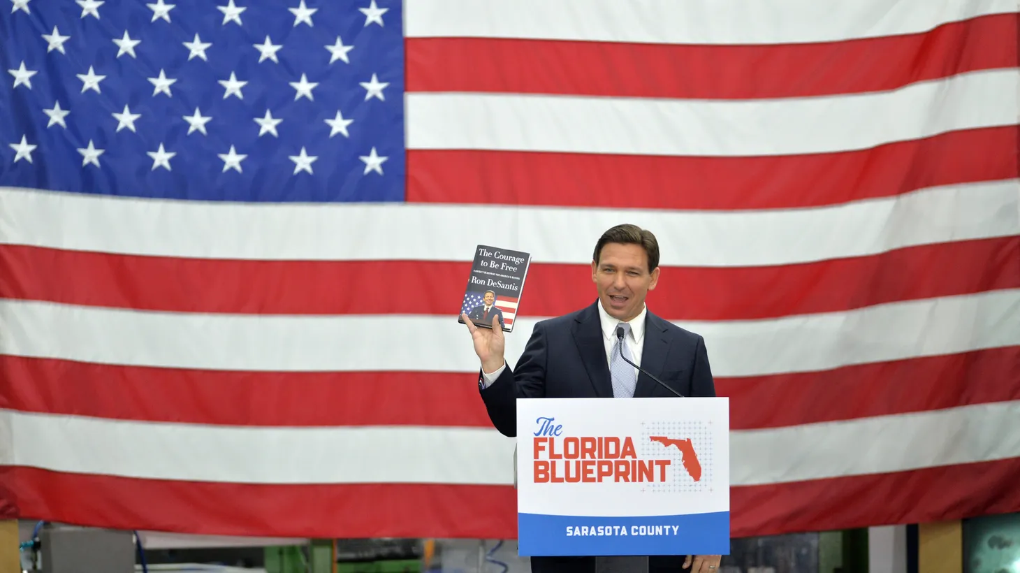 Florida Governor Ron DeSantis holds up a copy of his new book, "The Courage to be Free," during a campaign-style event at PGT Innovations in Venice, March 1, 2023.