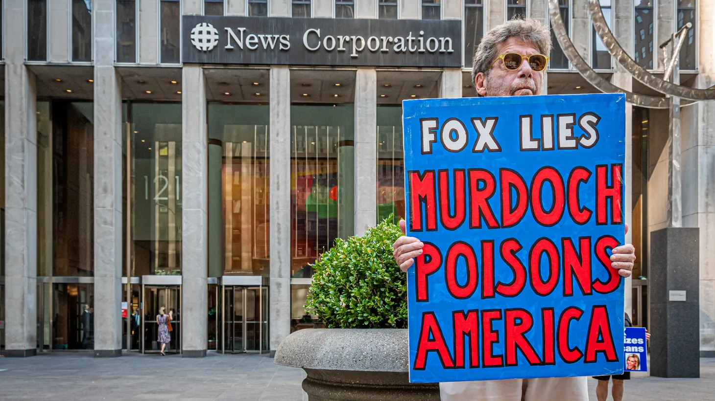 An activist holds a sign that says, “Fox lies, Murdoch poisons America,” outside Rupert Murdoch’s News Corporation building at 1211 6th Ave., August 9, 2022.