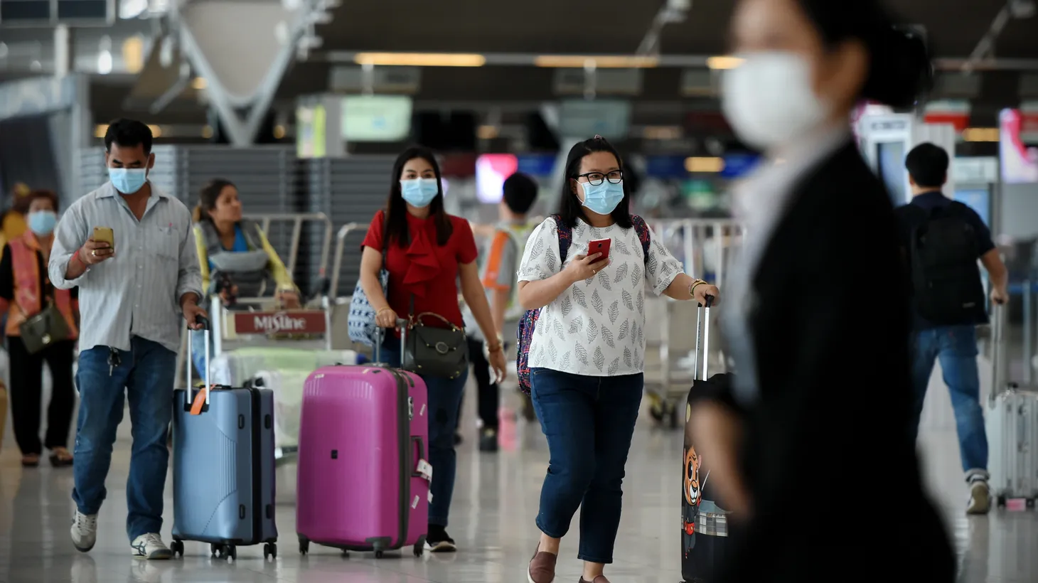 Air travelers wearing masks walk through Suvarnabhumi Airport in Thailand.