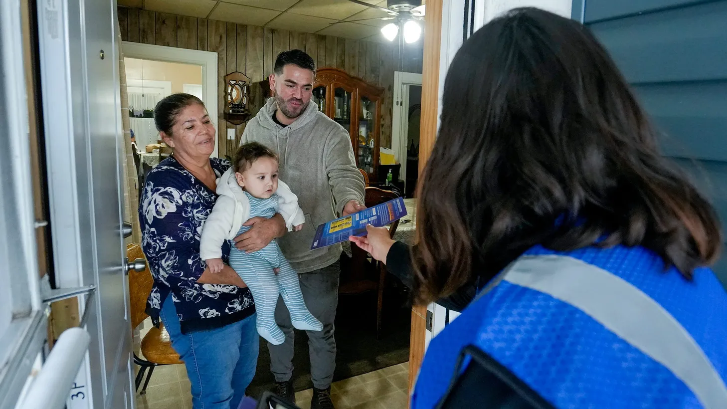 Deisy Espana with Voces de la Frontera hands a pamphlet to Danny Sanchez, his aunt Maria Sanchez, and his nephew Thiago Torres — as she goes door-to-door encouraging Latinos to vote, Oct. 6, 2022, Milwaukee.