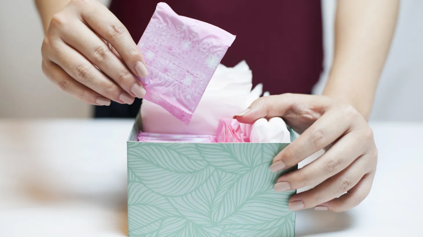 A woman pulls a menstrual pad out of a box. The pink tax is seen in the pricing of different products that are advertised towards men and women.