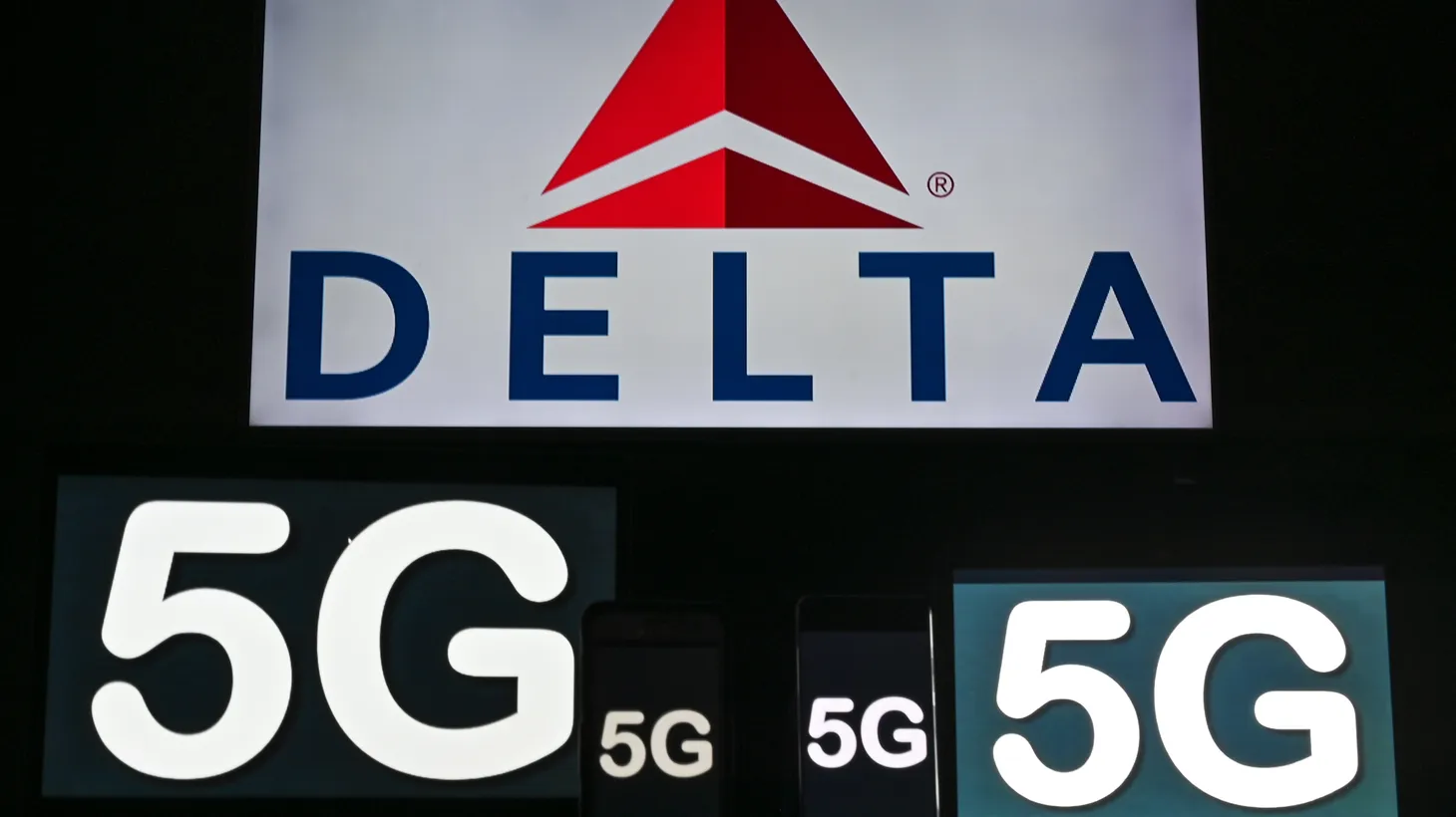 The 5G sign is displayed on screens of mobile phones and computers in front of the Delta Airlines logo.